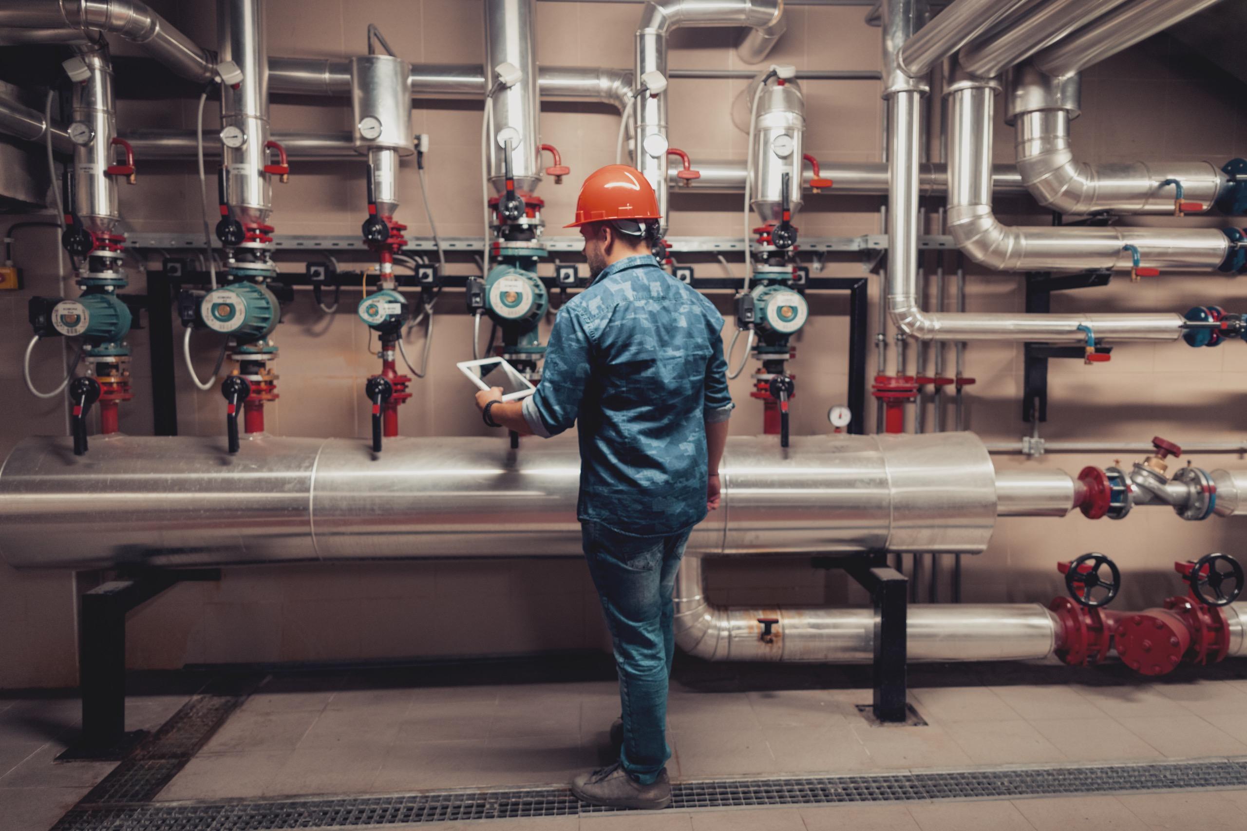 A worker in protective clothing is operating or inspecting industrial equipment, with a focus on maintenance tasks.